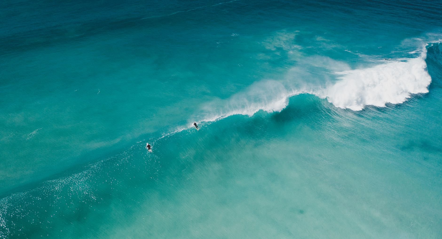 A breathtaking aerial view of surfers riding waves in vibrant turquoise waters of Shell Cove, Australia.